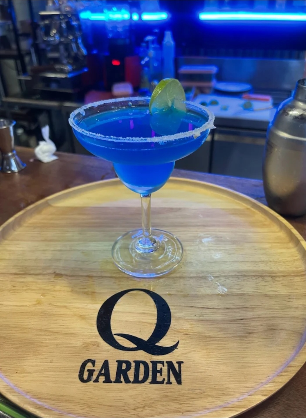 Signature blue cocktail on a wooden tray with Q Garden logo
