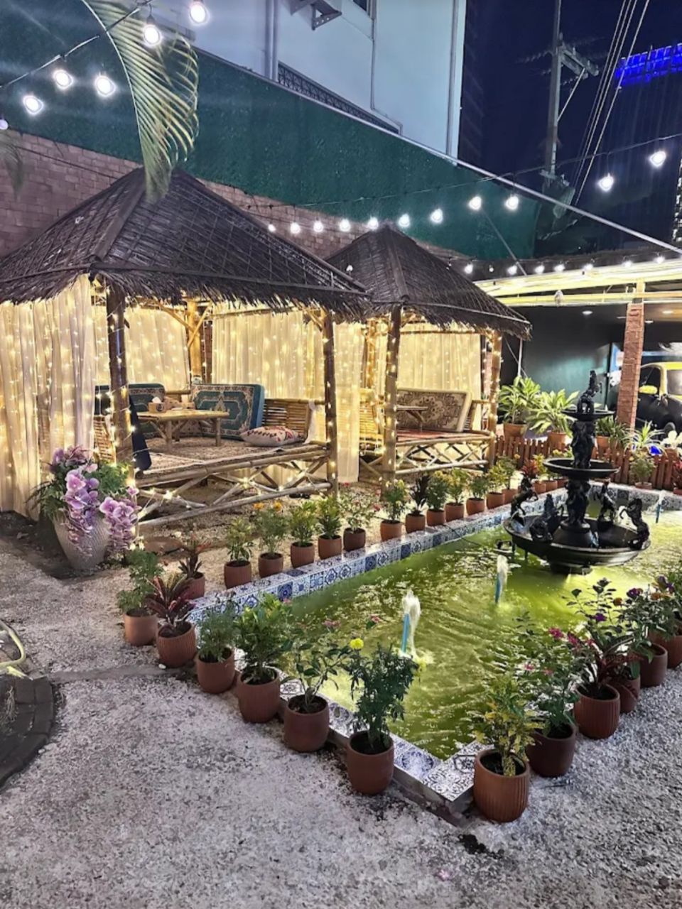 Q Garden's beautiful thatched gazebo with fairy lights and a garden fountain at night